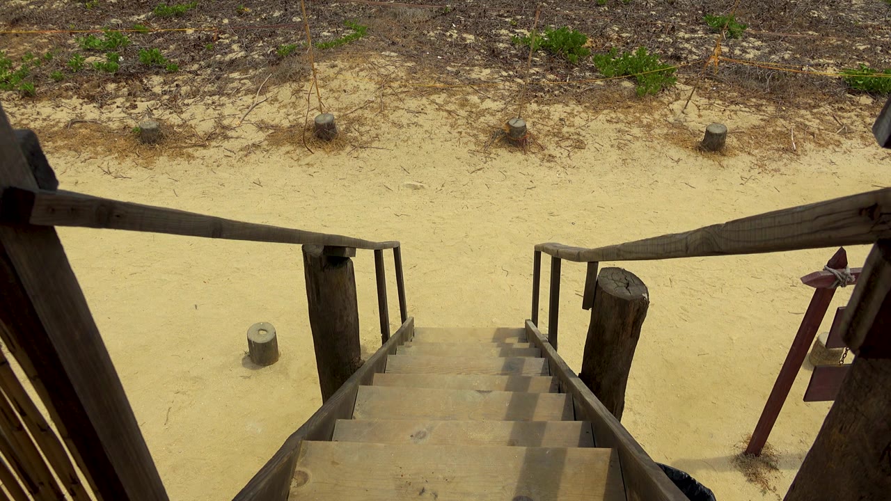 A slightly shifted view emphasizes the horizontal wooden rail over pale sand, dry weeds, and small posts in San Jose Del Cabo, Mexico, with no visible people.
