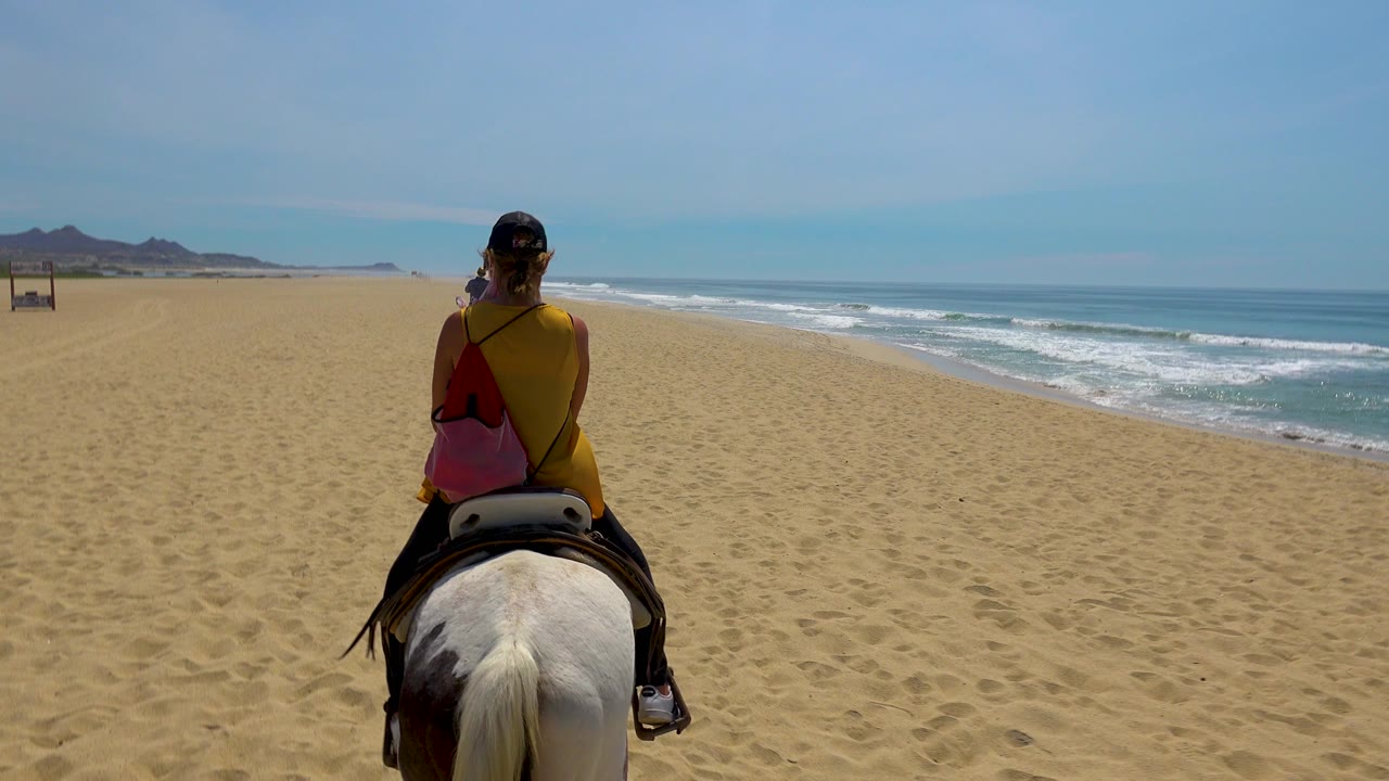 The rider remains centered on the horse as foamy waves break along the right edge and a wide stretch of empty sand fills the foreground in San Jose Del Cabo, Mexico.