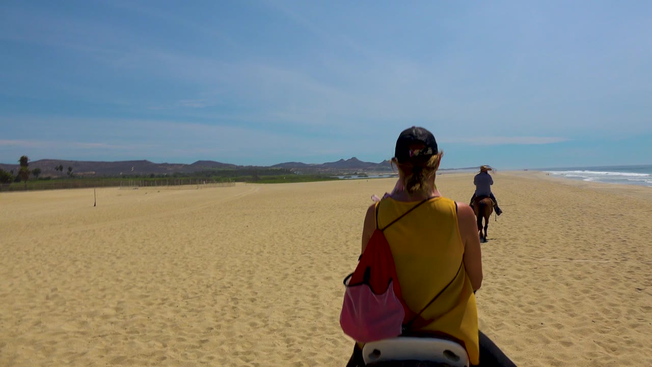 Beach horseback riders continue along open sand beside the shoreline.