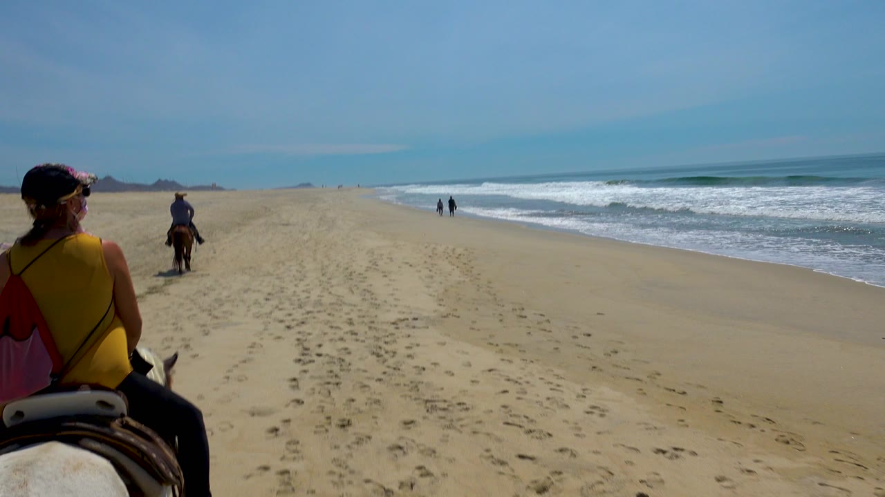 Riders on horses traveling down an open sandy beach.