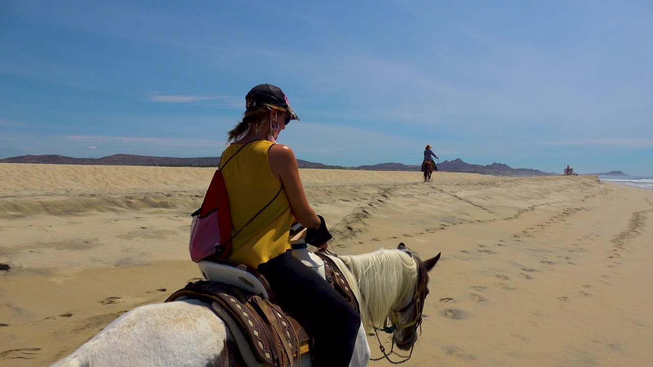 Close rider on a white horse crosses beach sand under blue sky.