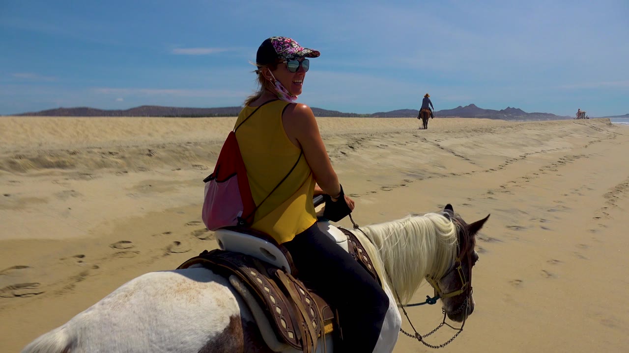 Smiling rider on a white horse looks back on a sandy beach.