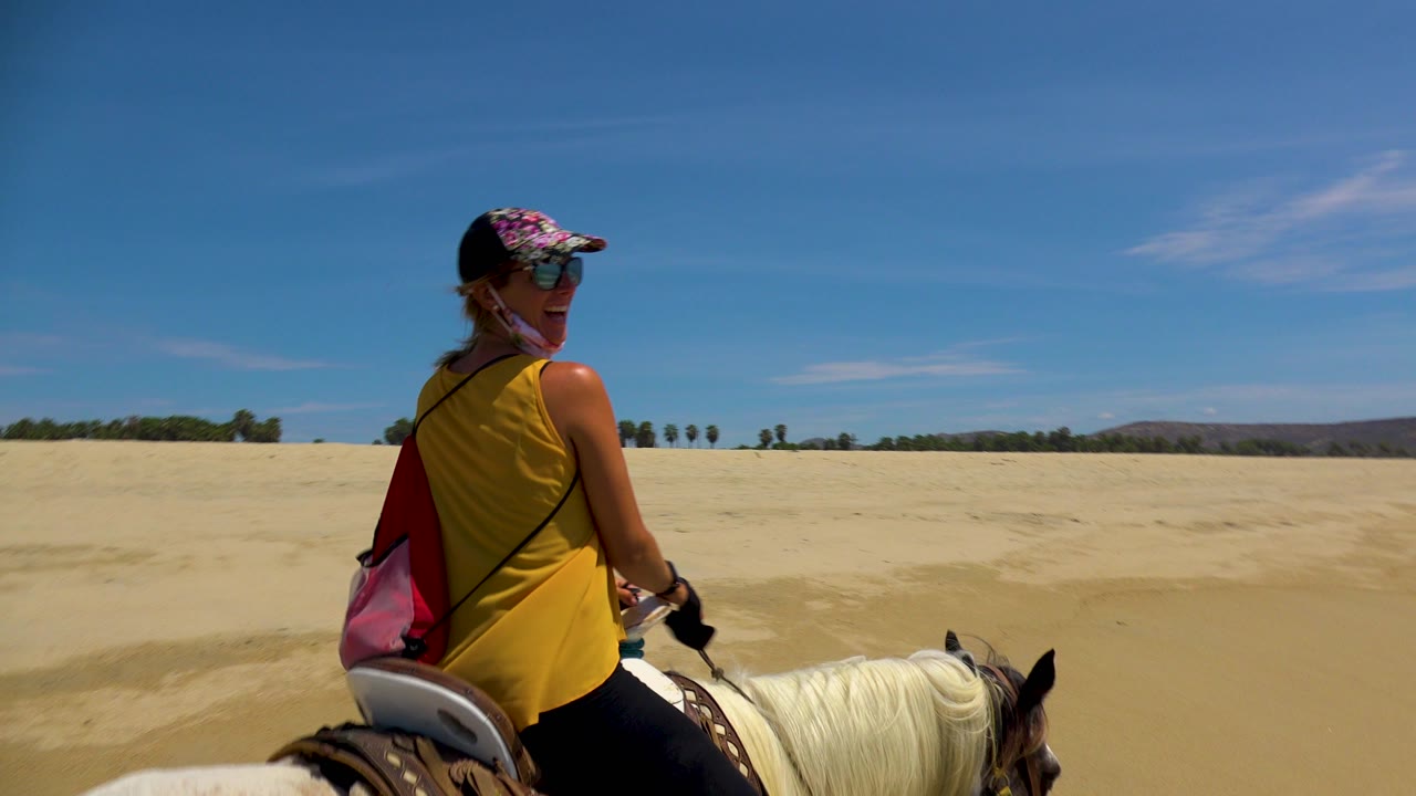 Smiling rider turning back on horseback at sandy beach