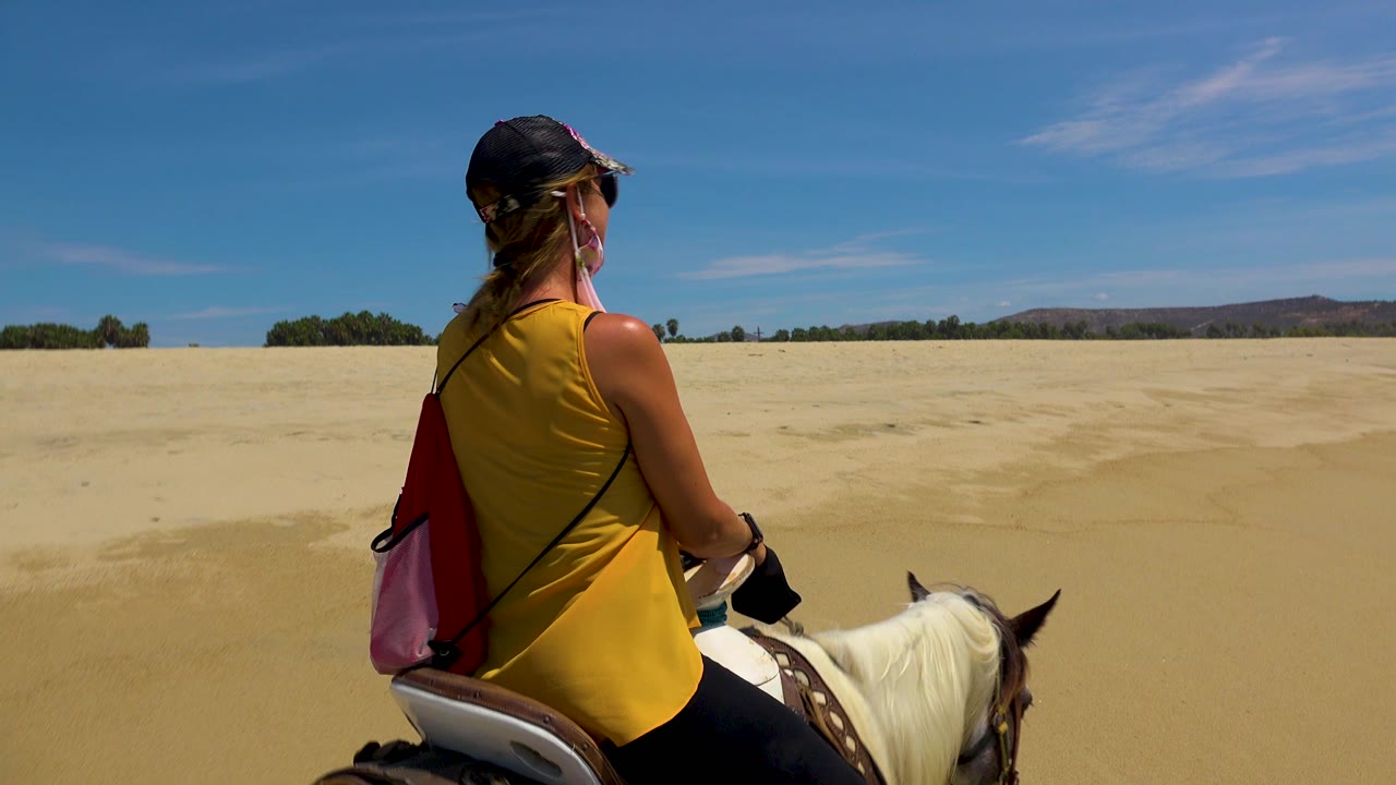 Horseback rider moving across open beach sand.