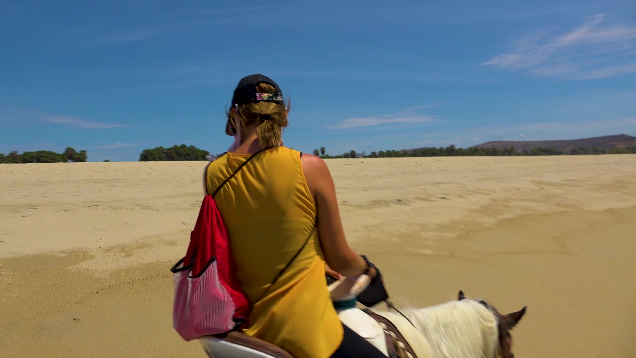 A rear view of the horseback rider at San Jose Del Cabo, Mexico shows the rider slightly farther right, with pale sand stretching to the horizon.