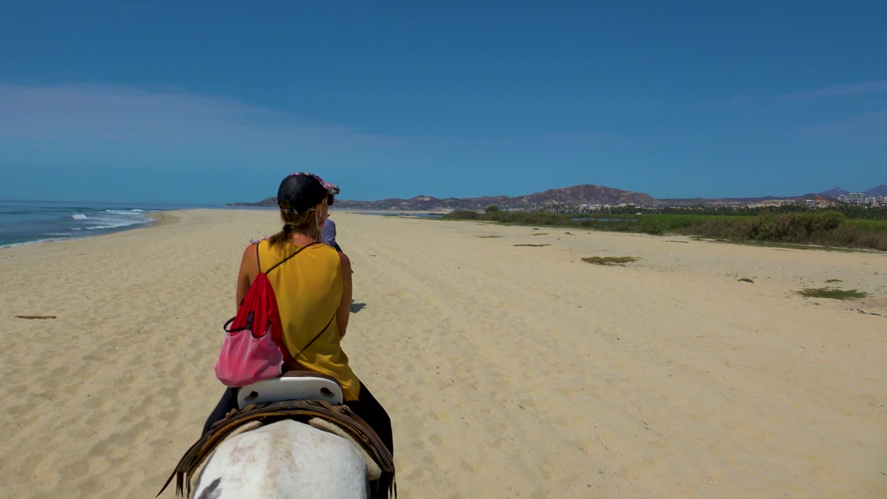 Rider on a white horse continues along the sandy beach with surf at left.