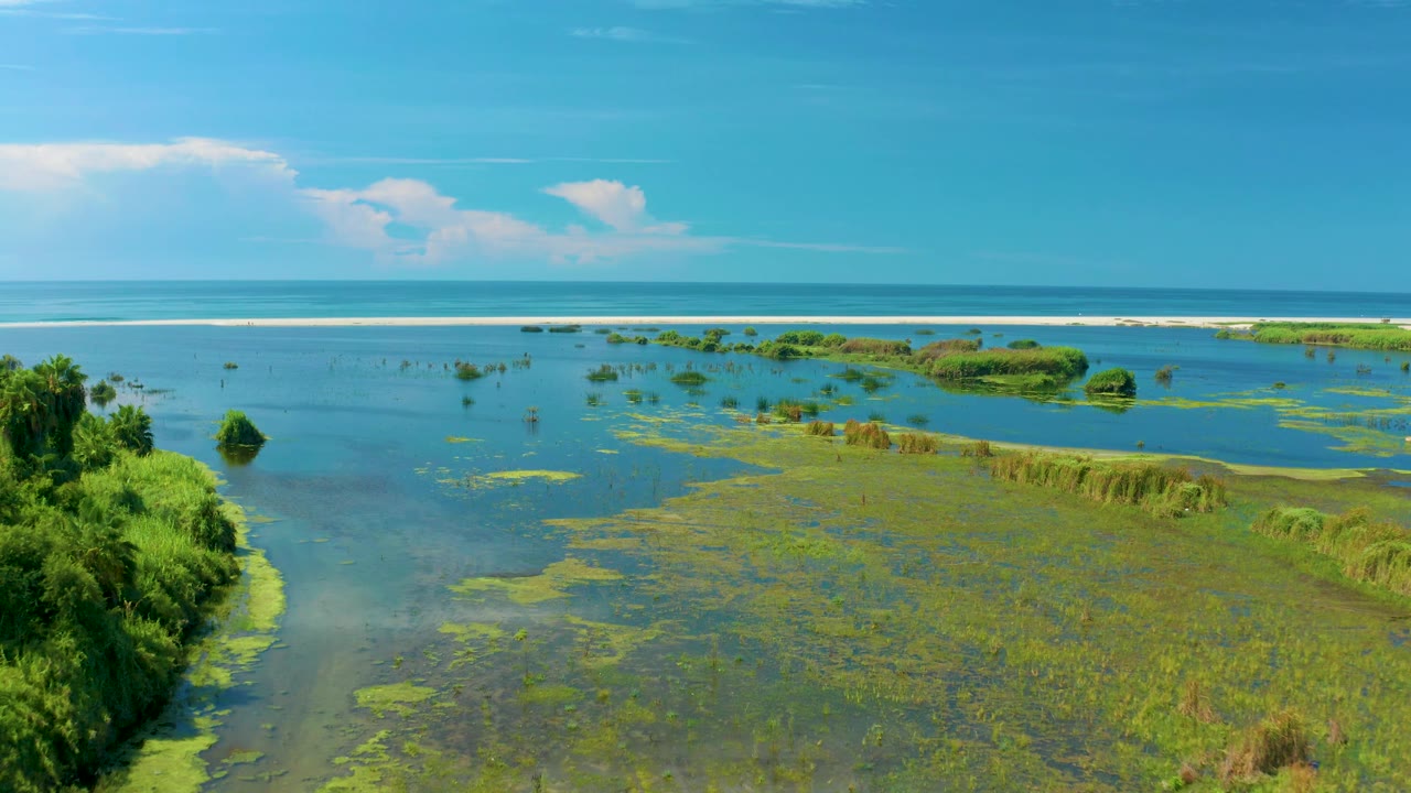 Frame two looks across green islands and shallow water in San Jose Del Cabo, Mexico, with the surf line stretching across the background and no visible people.