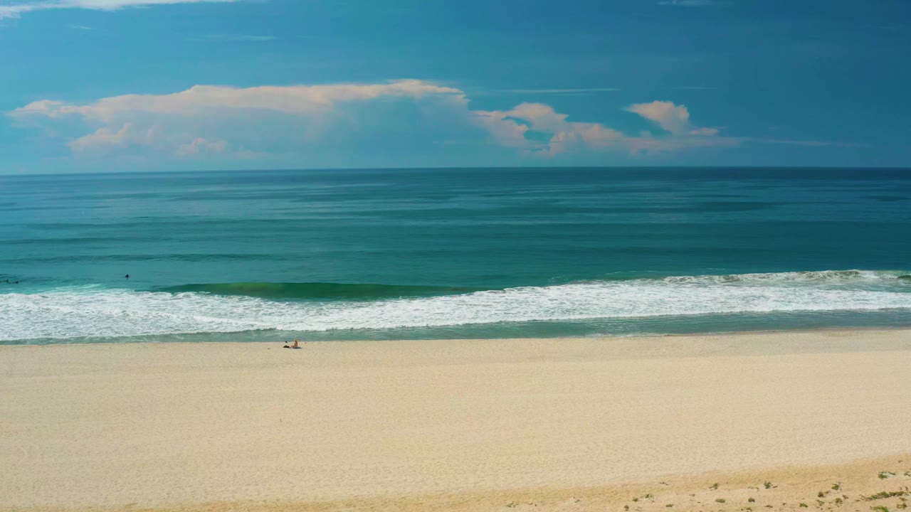 San Jose Del Cabo shoreline with a rolling white wave stretching across the frame, open sand below, blue-green ocean above, and no visible people.