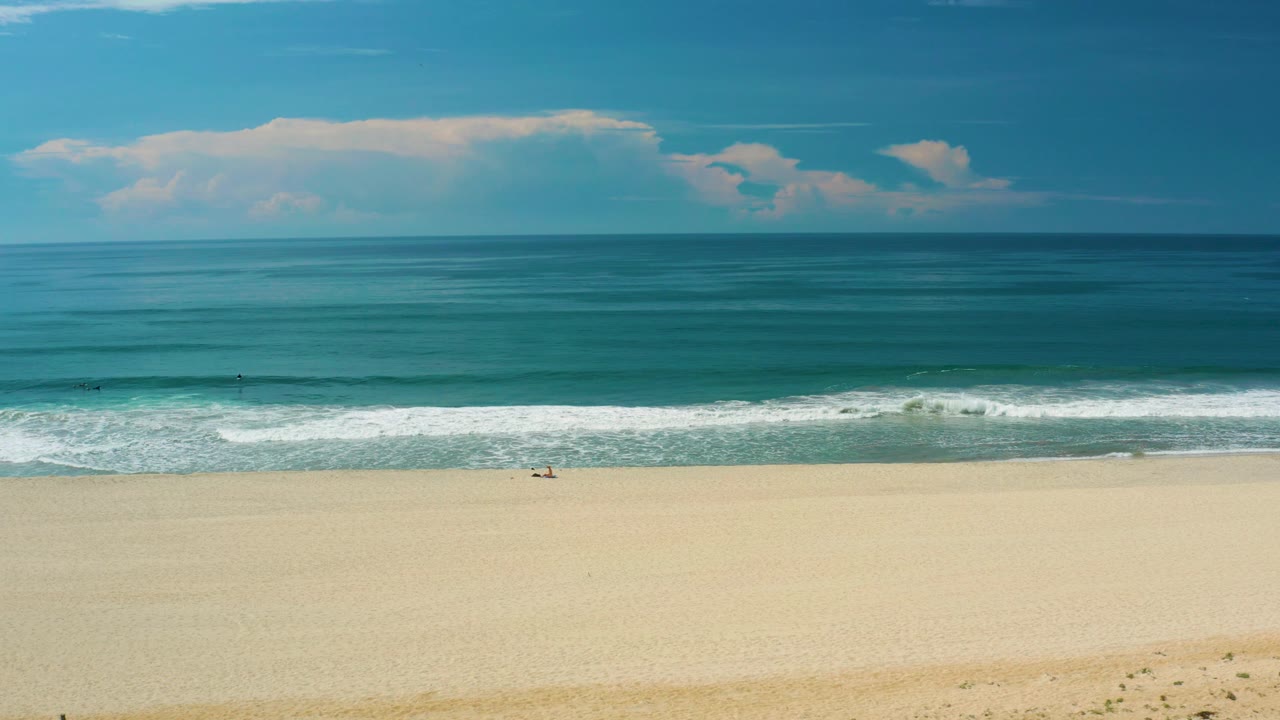 Beach shoreline under blue sky with low white clouds