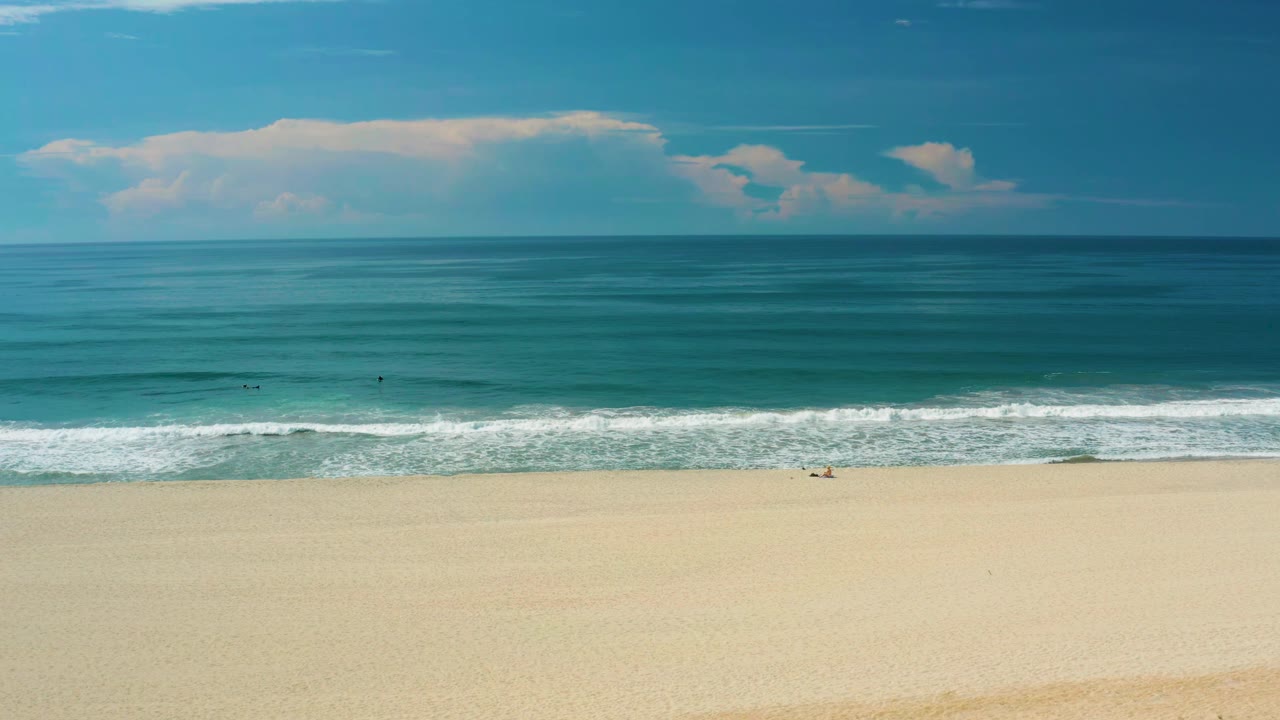 Ocean horizon over pale beach with a thin line of breaking waves.