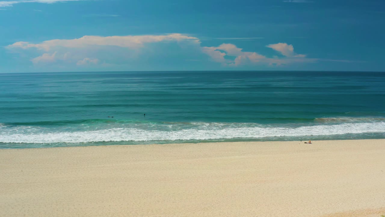 Ocean horizon over pale beach with surf rolling toward shore.