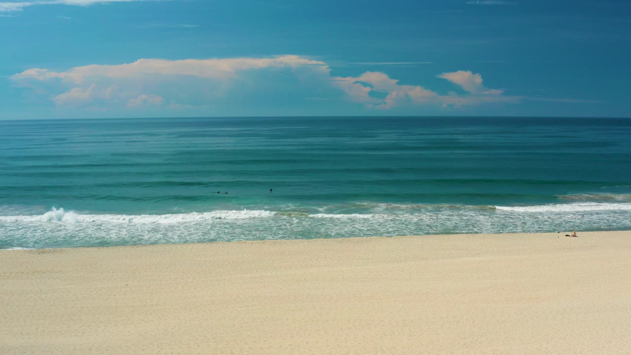 Wide beach, breaking surf, teal ocean, and blue sky.