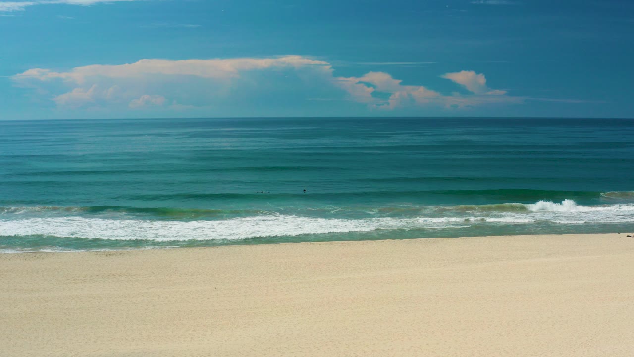 Wide beach shoreline with small waves under blue sky