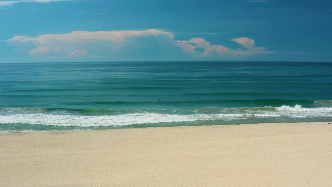 San Jose del Cabo shoreline with a low wave beginning to break across the center of frame, open sand below, blue water above, and no visible people.