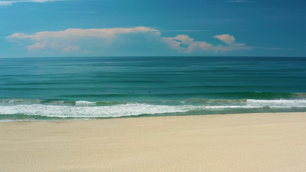 San Jose del Cabo beach with white foam spreading along the shoreline, calm turquoise water beyond, pale sand in front, and no visible people.