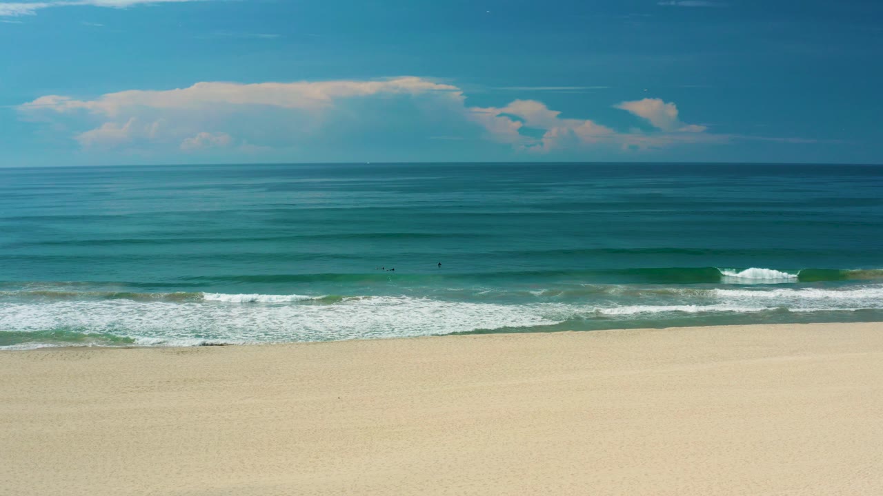 San Jose del Cabo ocean view with a clean horizon, broad blue-green water, a small breaking wave near shore, pale beach foreground, and no visible people.