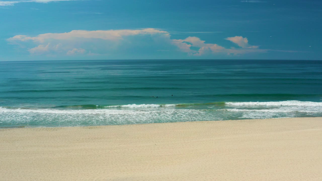 Wide beach and blue sea with white surf under a blue sky.