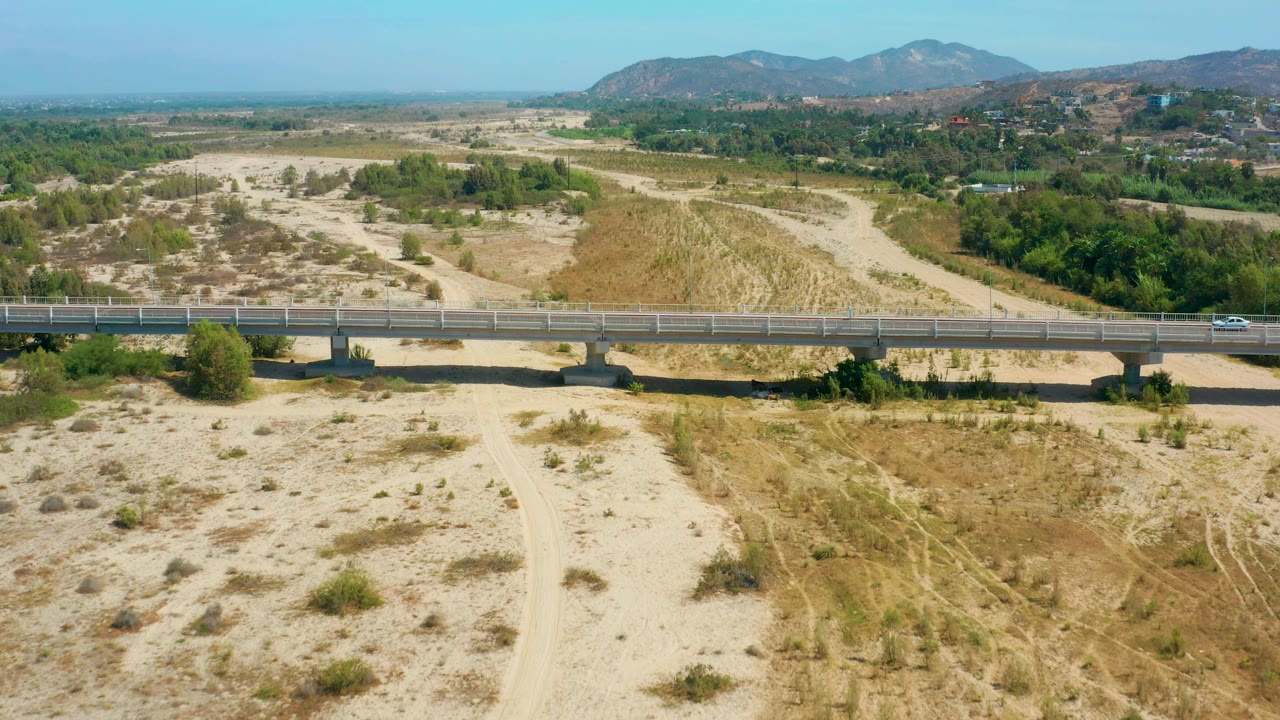 White car driving across a concrete bridge over dry sandy terrain.