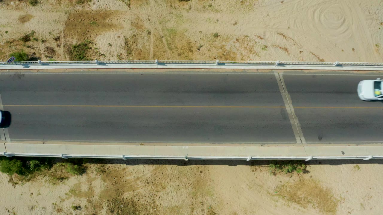 White car traveling on a concrete road beside sandy ground
