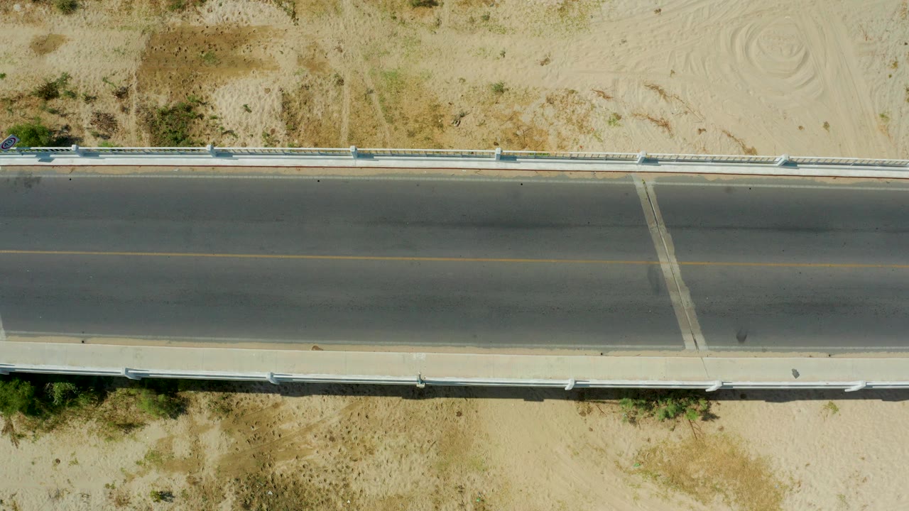 Straight overhead road with sandy shoulders and guardrails, no visible people.