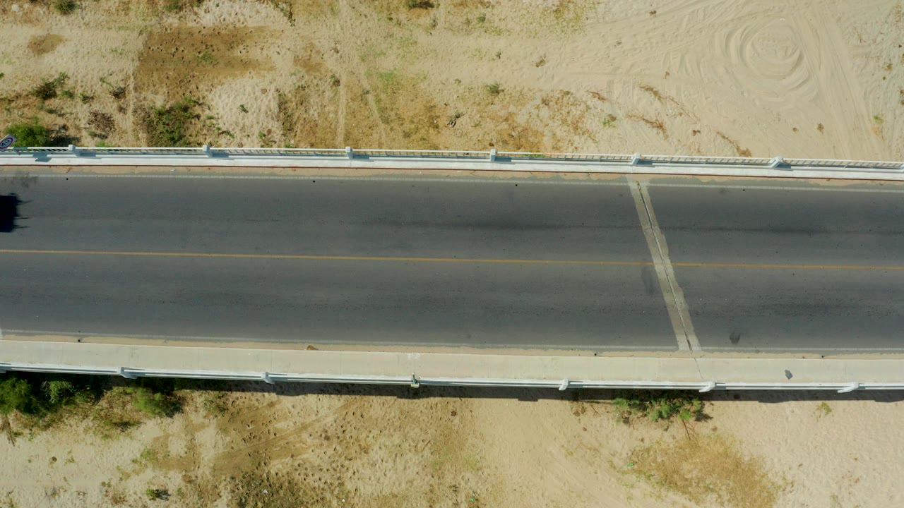 Overhead view of an empty desert highway bordered by sand and guardrails.
