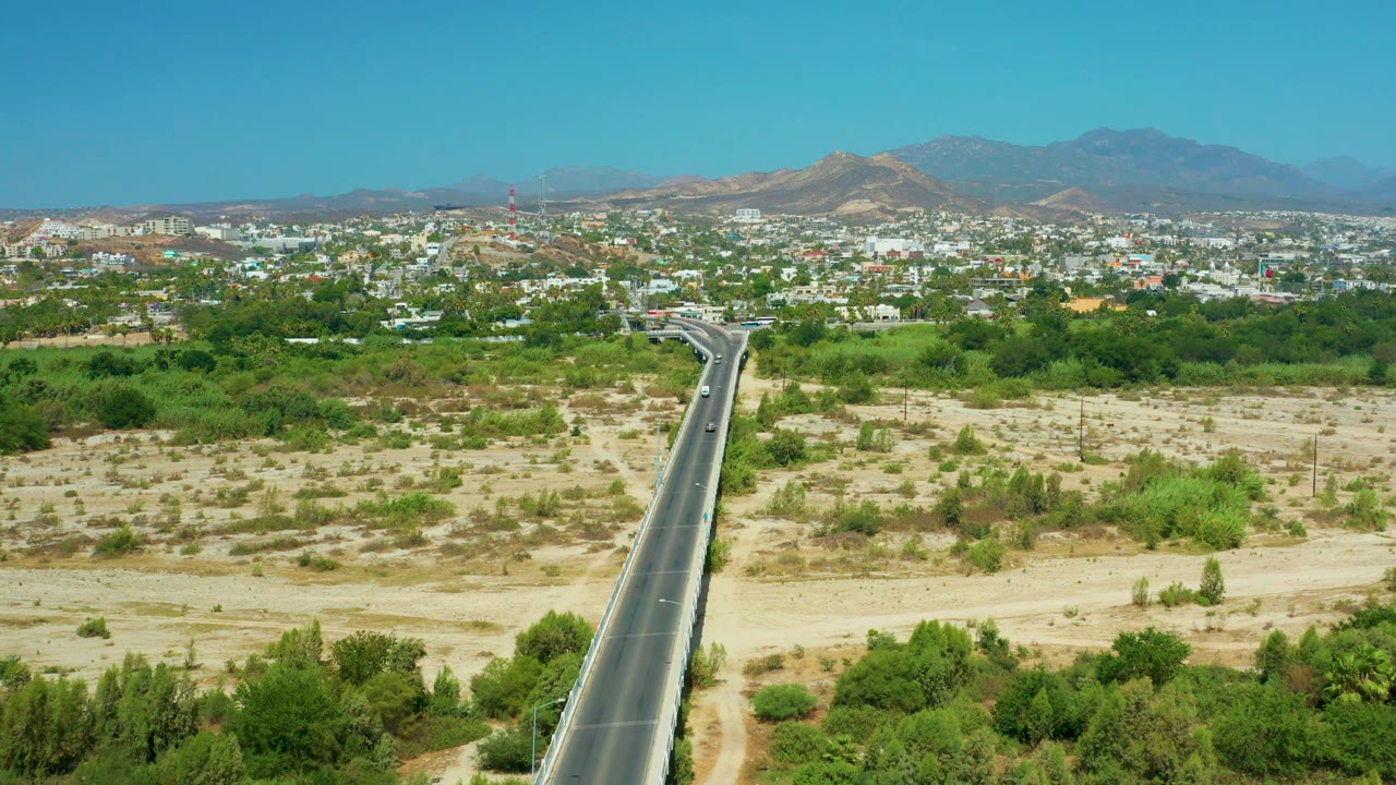Long highway line runs through desert vegetation toward a town skyline.