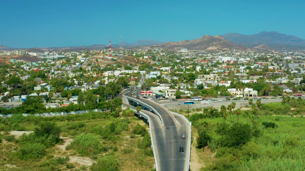 Road and bridge leading into a town with green foreground and hills behind.
