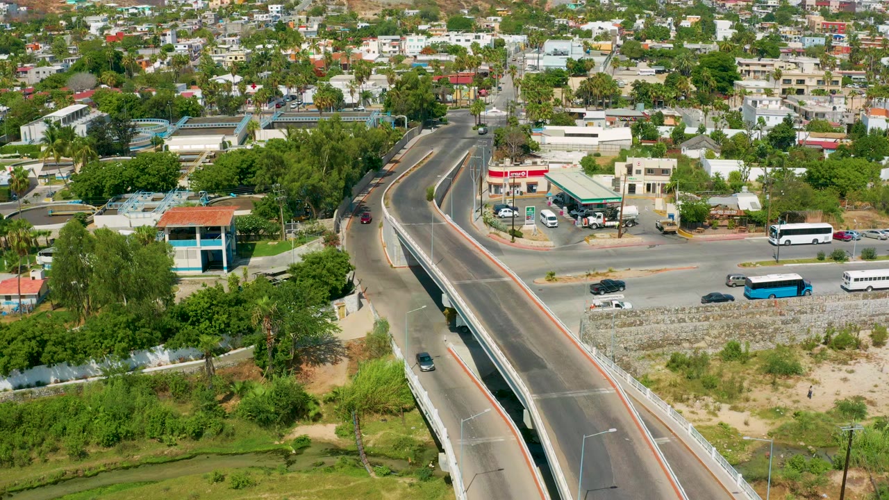 Aerial view in San Jose Del Cabo, Mexico, with a curving raised highway, trees, low buildings, buses, cars, and no visible people.