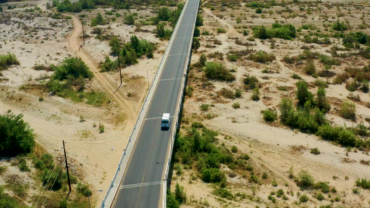 Vehicle farther along the road beside sandy open land.