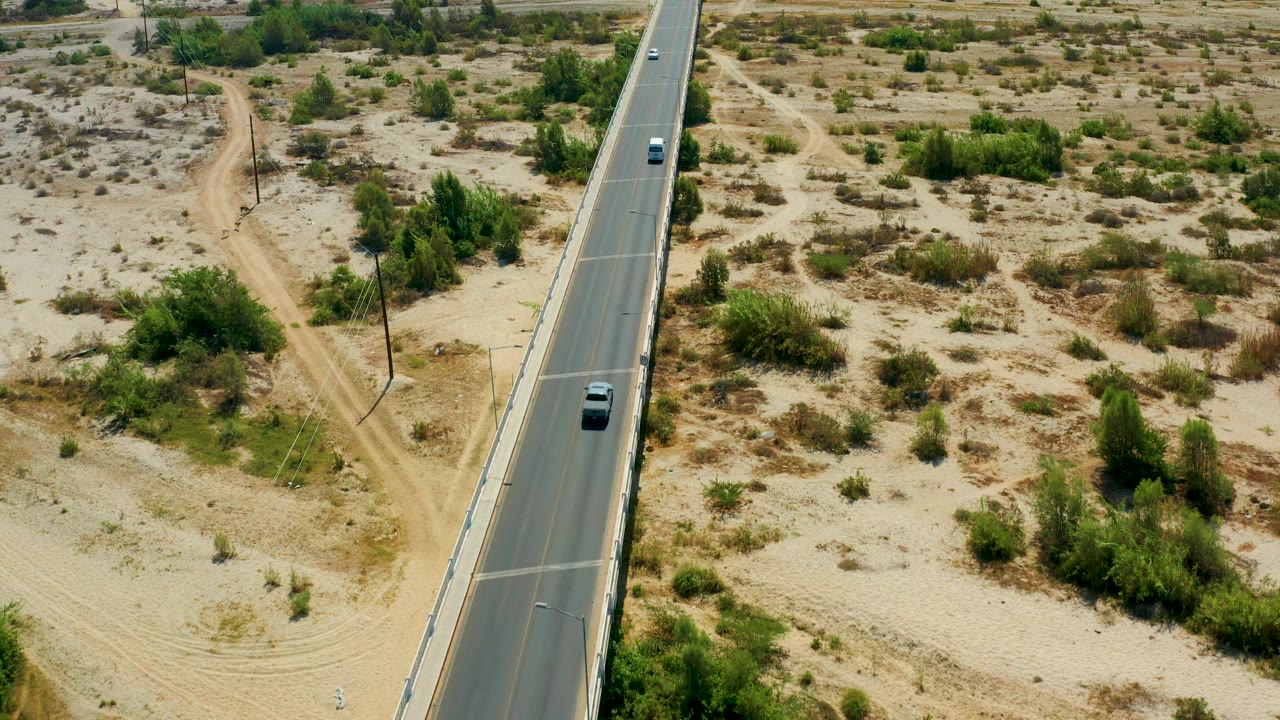Overhead angled view of a road beside sandy desert brush and a dirt access path.