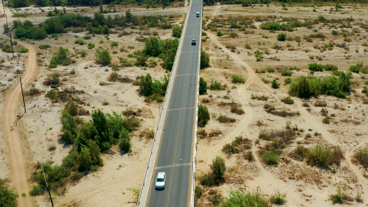 Aerial view in San Jose Del Cabo, Mexico, with the road running along the right side of frame, dirt tracks and scrubland to the left, vehicles on the pavement, and no visible people.