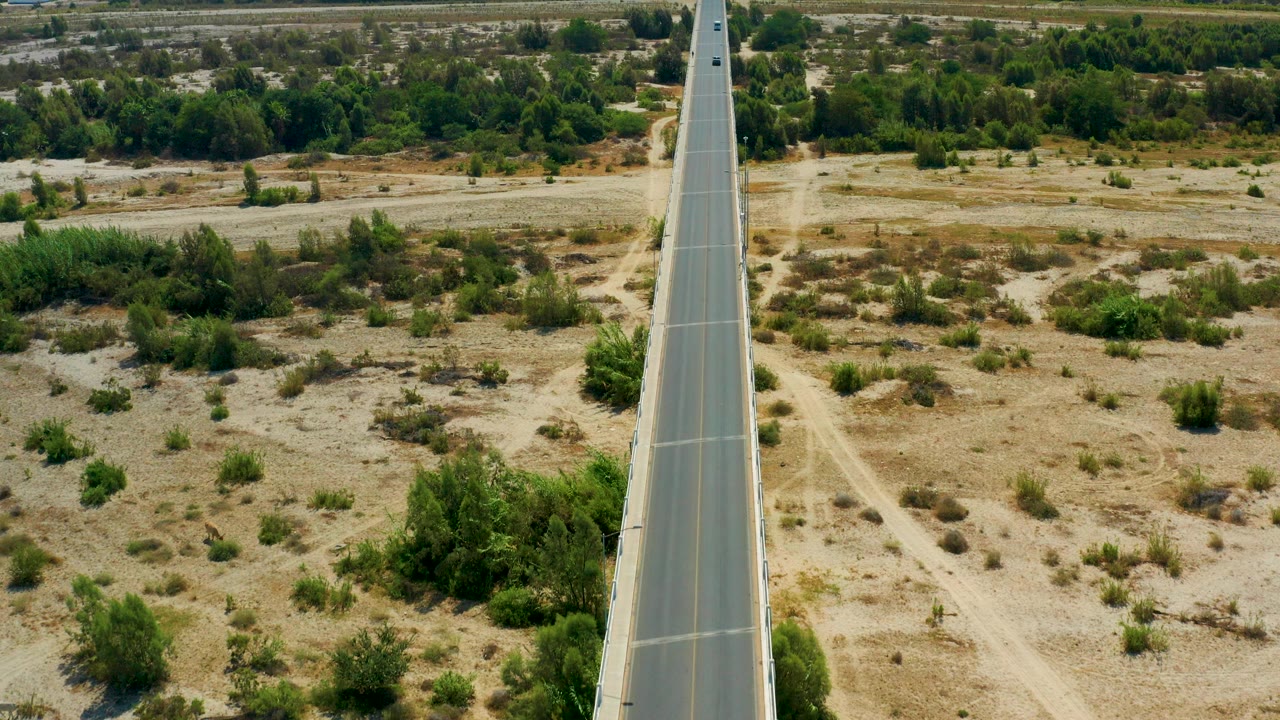 High aerial view over San Jose Del Cabo, Mexico, showing a straight paved highway centered between sandy scrubland and green vegetation, with no visible people.