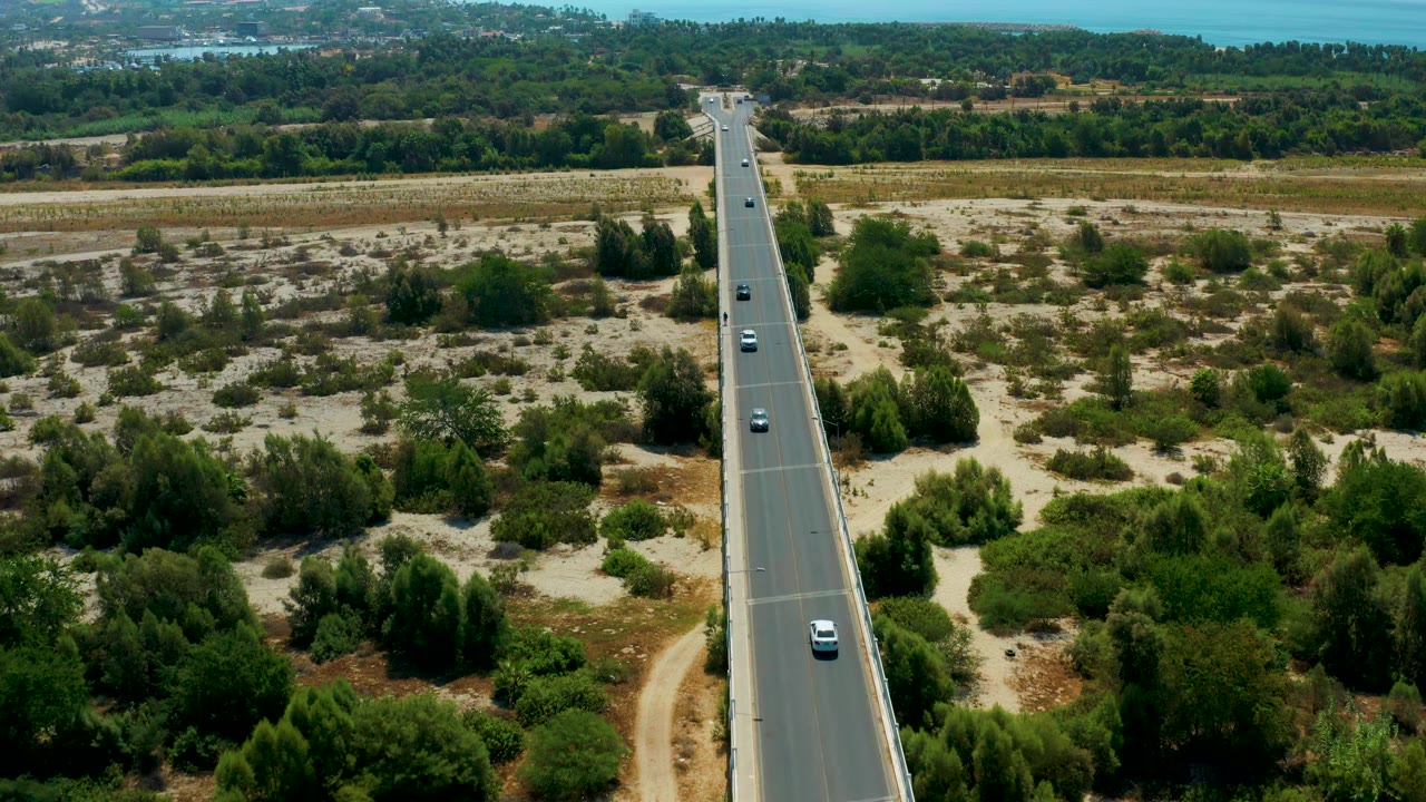 Aerial highway view with several cars moving through pale scrub and green vegetation.
