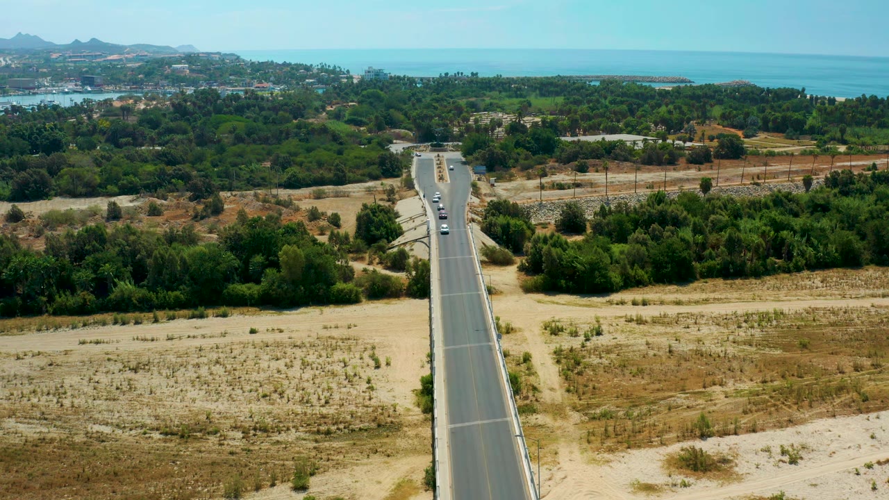 High road view with vehicles moving along a straight highway through scrubland.