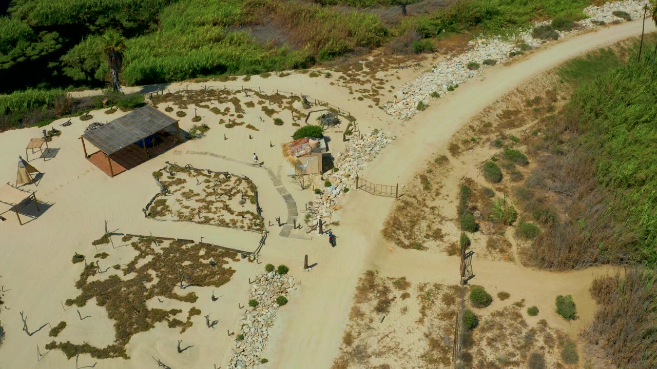 Aerial view of a roofed shelter beside sandy paths and scrub vegetation.