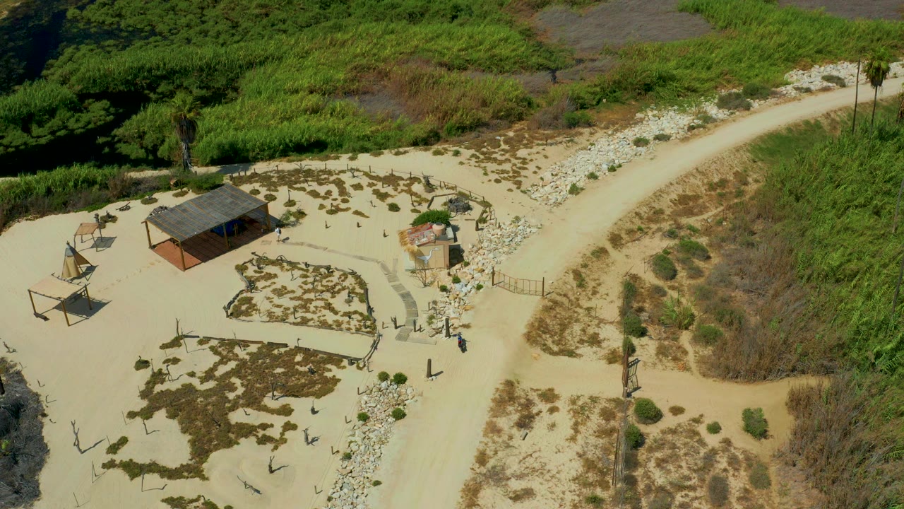 High aerial view of a small compound beside a pale dirt road and dense vegetation.