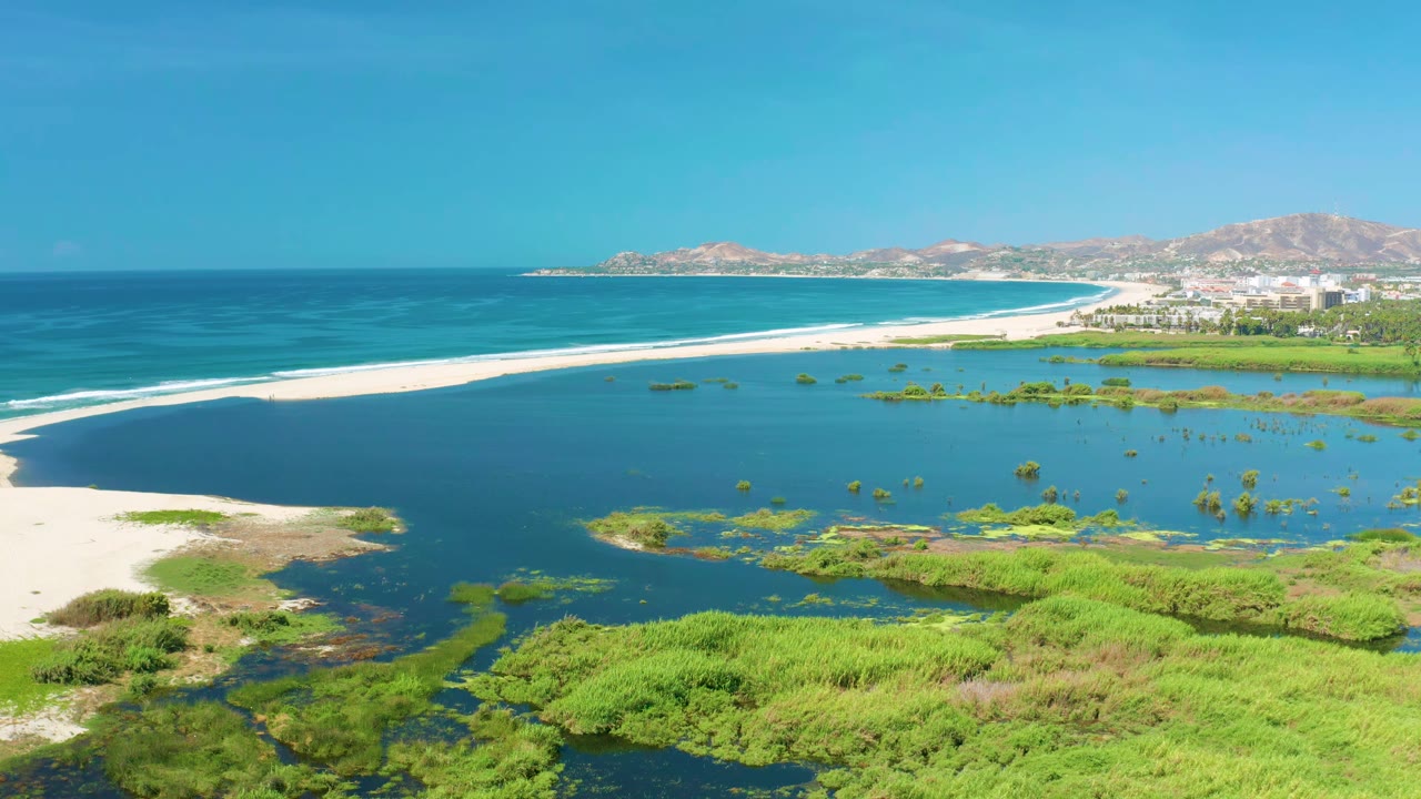 Aerial coastal frame in San Jose del Cabo, Mexico, showing the lagoon and sandbar slightly farther across the frame, with blue sea beyond and no visible people.