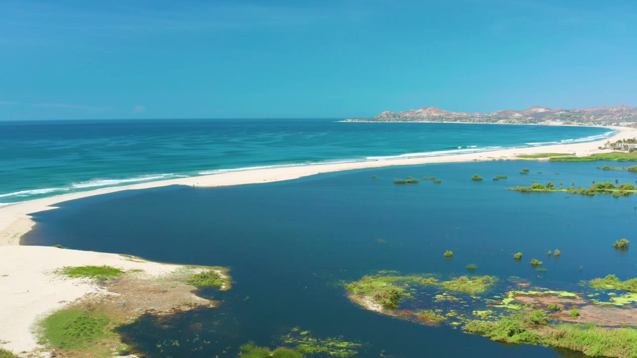 Lagoon and ocean separated by a long pale sandbar.
