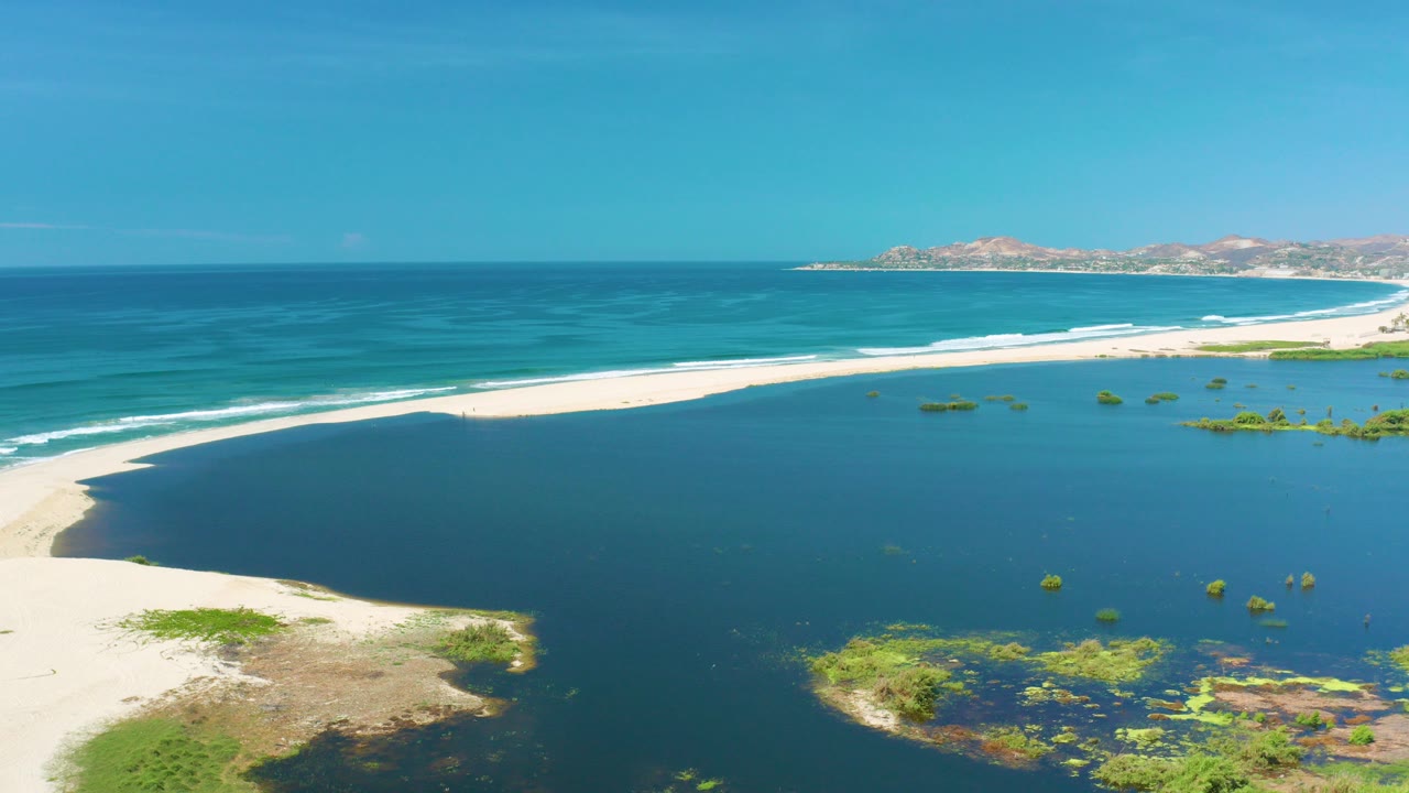 Opening aerial frame over San Jose Del Cabo, Mexico, showing a pale sandbar between deep blue ocean and darker lagoon-like water, with no visible people.