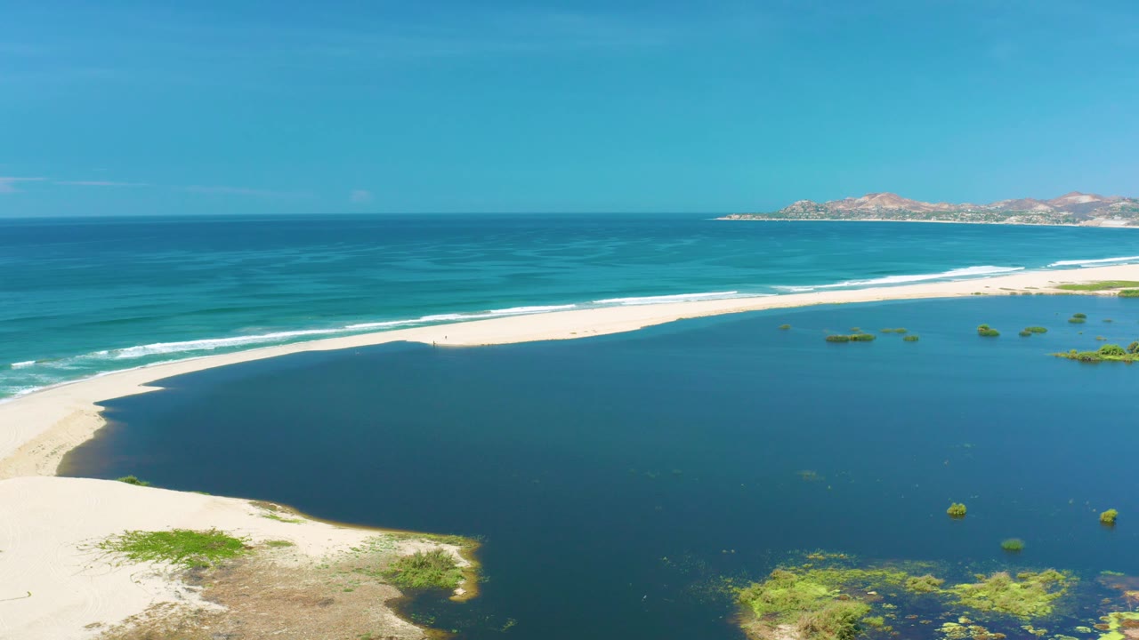 Bright aerial beach scene with blue water, white surf line, sandbar, and sparse green patches.