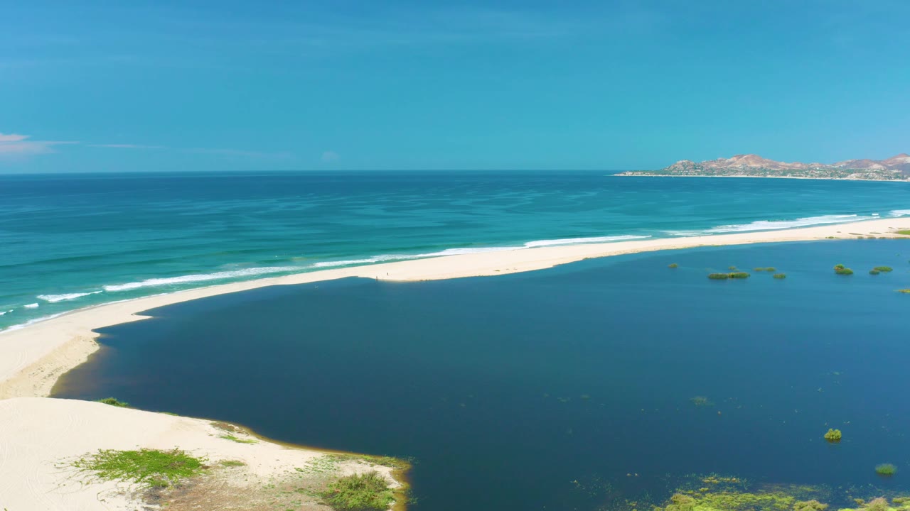 Aerial coastal view in San Jose Del Cabo, Mexico, with the white beach pushed toward the upper frame, dark water filling the foreground, teal ocean beyond, and no visible people.
