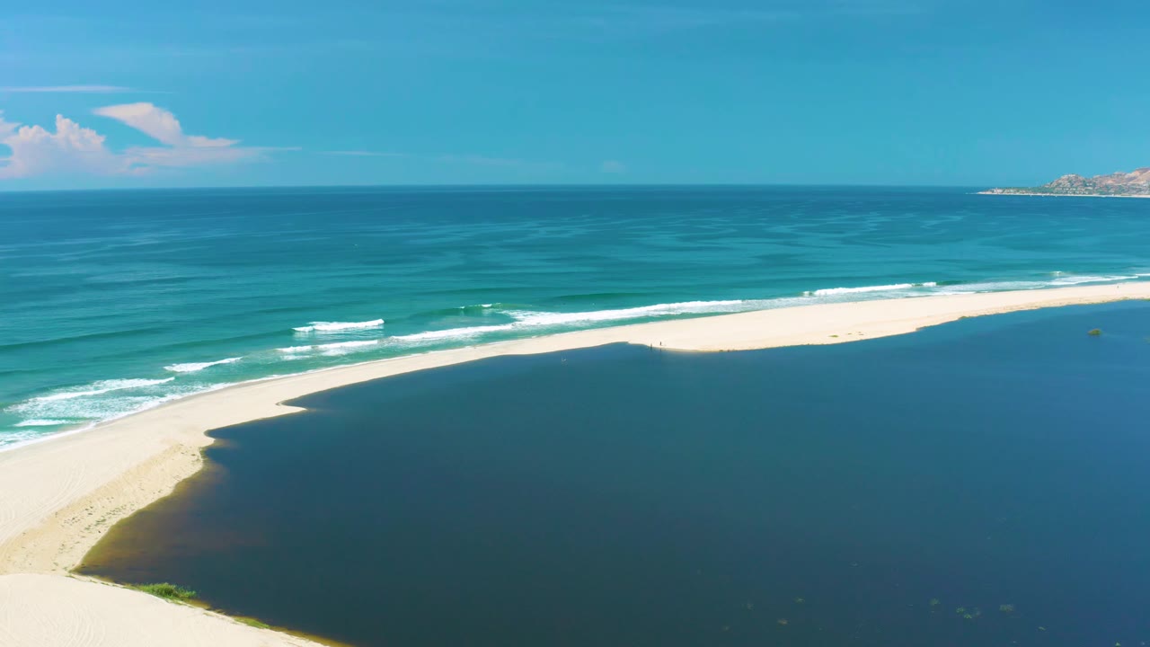 High aerial view in San Jose Del Cabo where white waves break along the ocean side of a curved sandbar, with darker water filling the foreground and no visible people.
