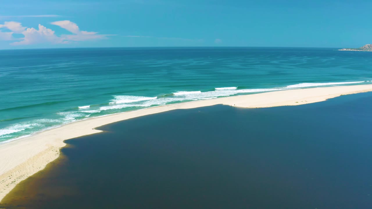 Aerial view in San Jose Del Cabo with white wave bands rolling toward a bright sandbar, darker water in the foreground, open ocean beyond, and no visible people.