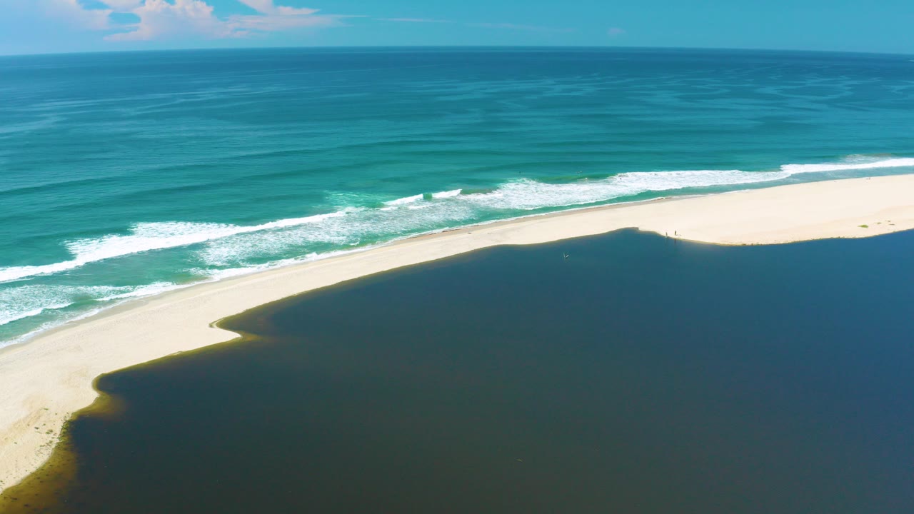 High aerial frame in San Jose Del Cabo, Mexico showing turquoise surf above a pale sand strip and dark coastal water in the foreground, with no visible people.
