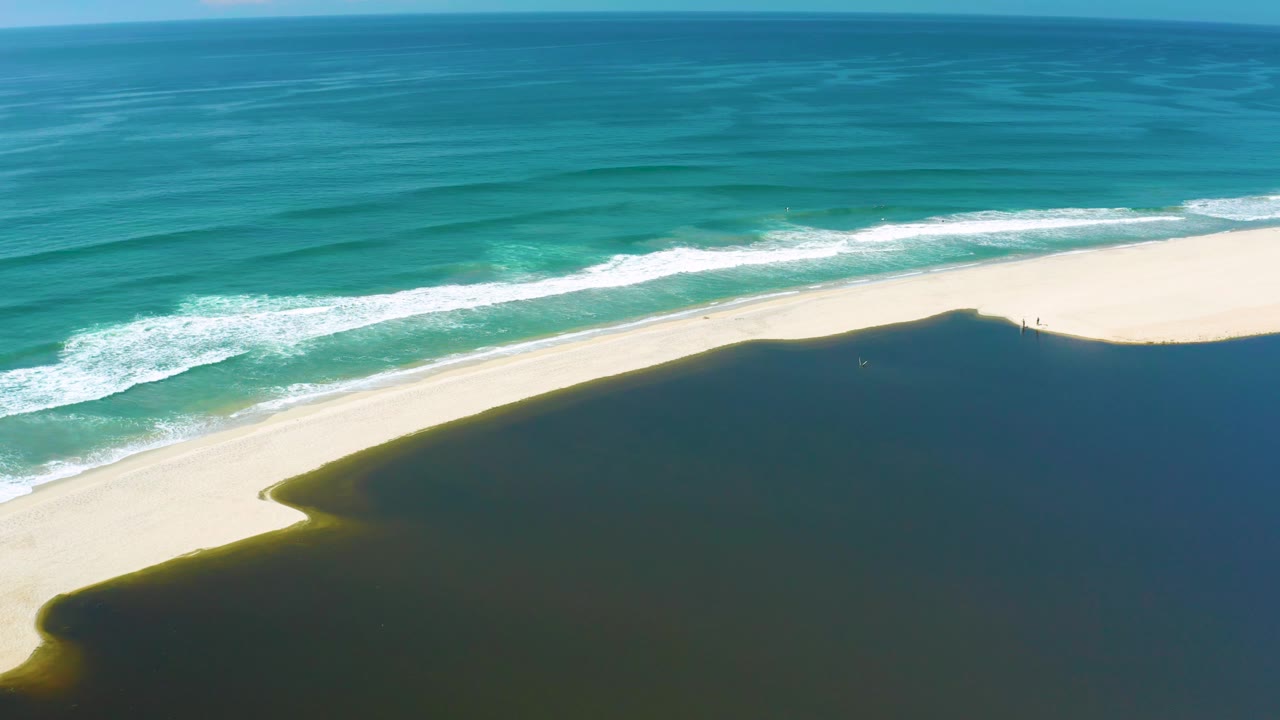 Aerial view in San Jose Del Cabo, Mexico with white wave bands advancing toward a pale sandbar above dark inlet water, with no visible people.