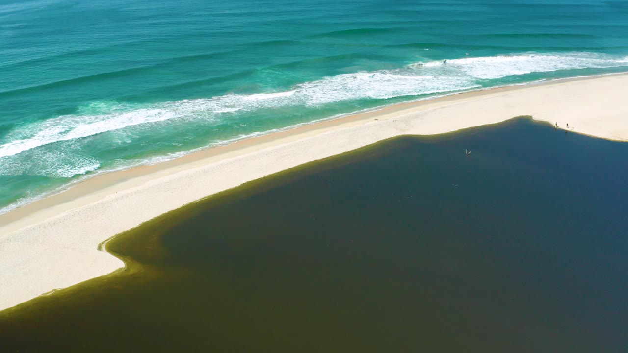 Aerial frame from San Jose del Cabo, Mexico, showing turquoise surf above a pale diagonal beach and dark green-blue water below, with no visible people.