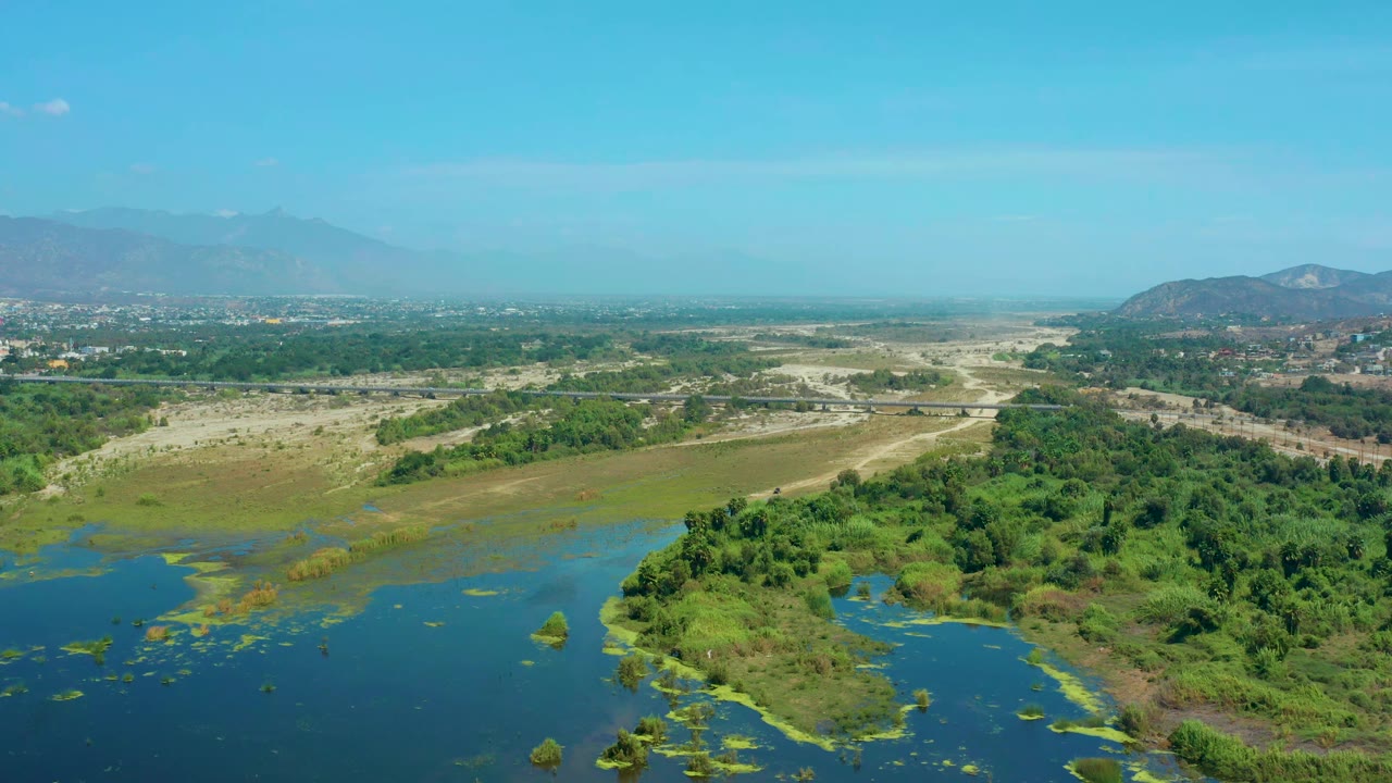 High view over water, wetland vegetation, dry flats, and hazy mountains