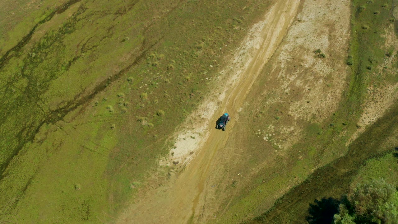 High overhead view in San Jose Del Cabo, Mexico with the dark vehicle centered on the dusty track and dry scrub patches around it, with no visible people.
