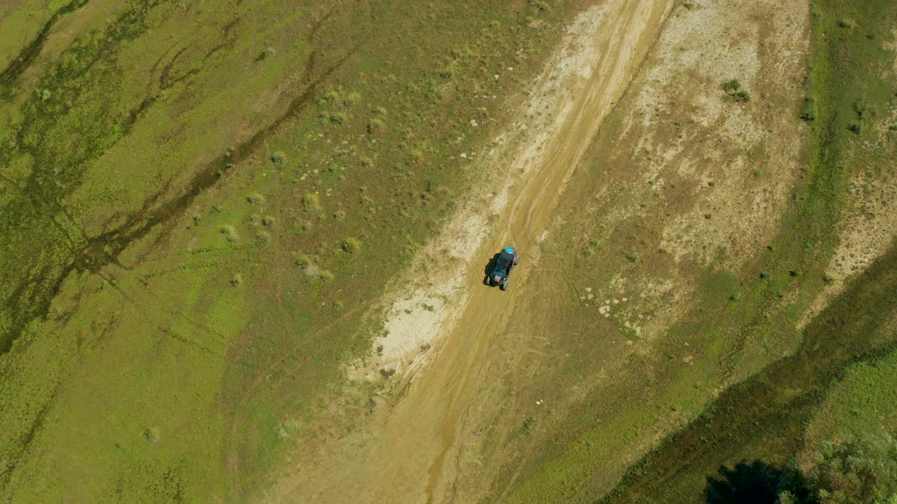 Overhead San Jose Del Cabo, Mexico view showing the lone dark vehicle slightly right of the dirt track center, with exposed pale soil and no visible people.