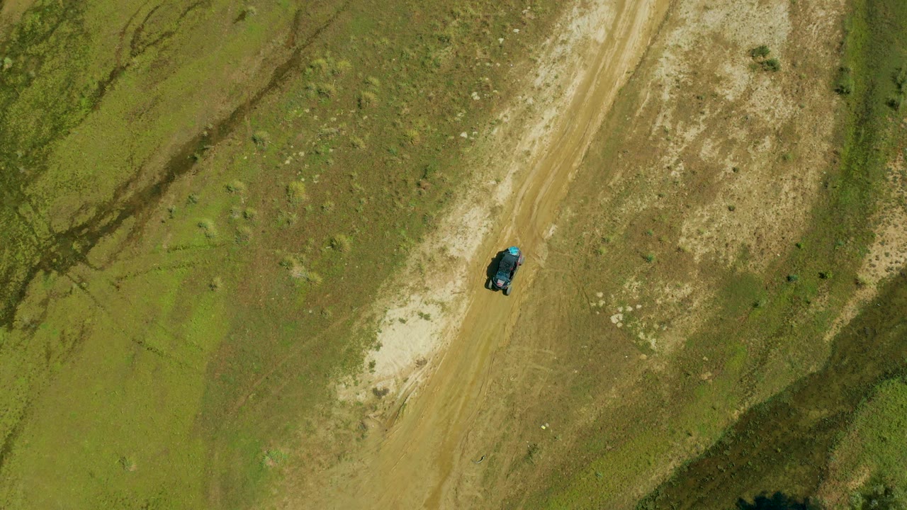 Top-down frame from San Jose Del Cabo, Mexico with a dark vehicle on a pale road, darker drainage-like marks in the scrub, and no visible people.